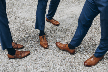 men in suits and leather shoes stand on a gravel park path