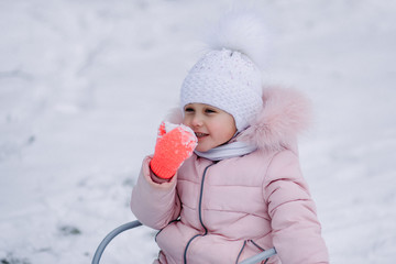 little girl in winter eats snow in nature