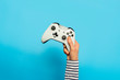 © Alex - Female hand hold a gamepad on a blue background. Concept of the game, e-sports, leisure, gaming industry, video games. Banner. Flat lay, top view