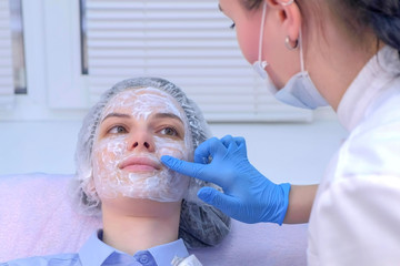 Cosmetologist is applying cream with anesthesia on patient's face skin before biorevitalization procedure. Woman in beauty clinic with doctor beautician preparing to treatment using numbing cream.