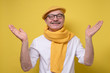 © Viktor Koldunov - Hispanic senior man in glasses and yellow beret and scarf spreading hands up welcoming his friend looking with a smile at camera. Studio shot. Positive facial human emotion.