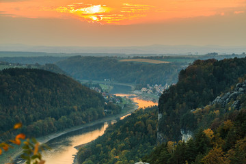 Magnificent sunset with a view over the Elbe valley in the Saxon Switzerland National Park. Landscape of the Bastei bridge with rocks, trees and forests in the autumn mood with an orange horizon