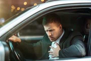 Wall Mural - young businessman suffers terrible heartache while siting in his car with open window, safety driving concept