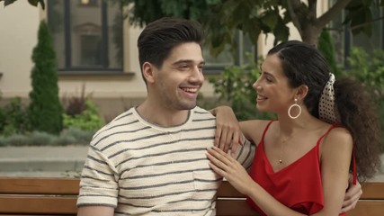 Canvas Print - A happy smiling woman is kissing her boyfriend while sitting on bench at city street