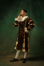 Posing Thoughtful. Portrait Of Medieval Young Man In Vintage Clothing Standing On Dark Background. Male Model As A Duke, Prince, Royal Person. Concept Of Comparison Of Eras, Modern, Fashion.