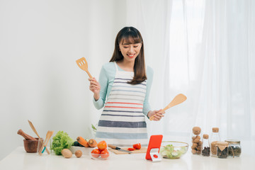 Beautiful young asian woman reading cooking recipe or watching show while making salad