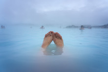 Feet Of A Woman Bathing In The Blue Lagoon Next To Reykjavik With People Bathing In This Natural Hot Spring
