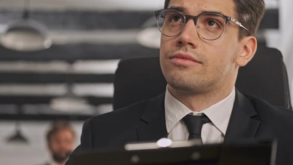 Poster - Close up view of serious pensive businessman in formal suit and eyeglasses holding clipboard and looking away while sitting in office