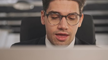 Poster - Close up view of Calm businessman in formal suit and eyeglasses using laptop computer while sitting in office