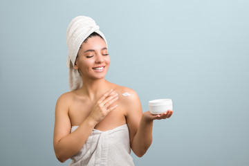 beauty woman in towel holding white jar with cream and caress her skin. grey background