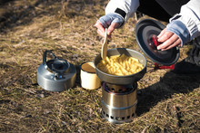Close Up Of Hiker's Hands Cooking Pasta On Portable Wood Stove. Cooking Pasta In Mountains