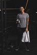 © LIGHTFIELD STUDIOS - happy african american girl with tattoo holding sports bottle with water and standing in gym