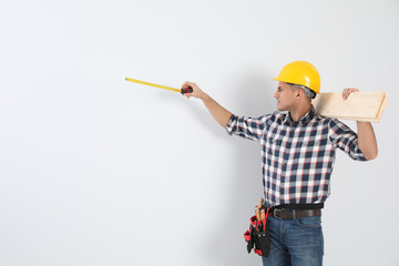 Canvas Print - Handsome carpenter with wooden planks and measuring tape on light background. Space for text