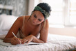 © JustLife - Beautiful woman in bed. Pretty girl writing in her diary.