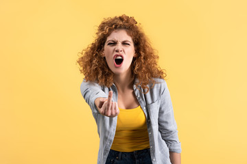 aggressive redhead woman yelling and showing middle finger, isolated on yellow