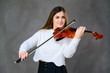 © Вячеслав Чичаев - Concept musician violinist. Portrait of a pretty brunette girl in a white sweater playing the violin on a gray background