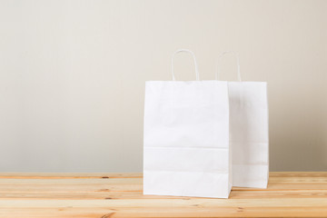 An empty paper bag with handles for shopping, on the front right side of a table in light wood with a light wall background, providing copy space on the left.