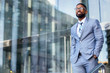 © elnariz - Young accomplished african american CEO business founder entrepreneur, stylish suit and glasses standing confidently at workplace office building