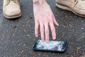 Man catching broken smartphone from the ground. Damaged mobile phone with cracked touch screen