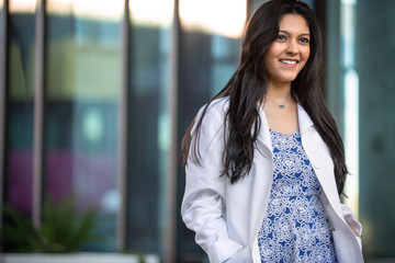 Wall Mural - Candid lifestyle portrait of a female medical professional in a white coat walking outside workplace