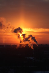 Wall Mural - red sun at sunset or dawn at dusk low above the horizon shrouded in smoke from the chimneys of the p