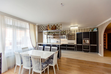 Wall Mural - Large Kitchen-living room in the cottage with kitchen and dining area. Luxury style. The kitchen is black and white, and the dining table and chairs are white. 