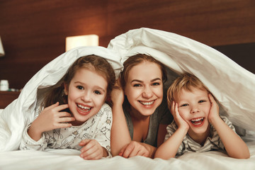 Wall Mural - happy family mother and children son and daughter laughing, playing in bed