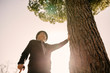 © Westend61 - Old man with cane, leaning on tree in park