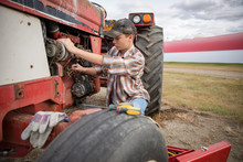 Teenage Boy Farmer Fixing Tractor On Farm