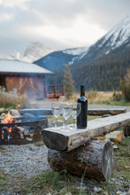 Wine Bottle And Wine Glasses By Campfire Outside Mountain Cabin, Rocky Mountains, Canada