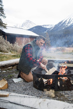Man Building Campfire Outside Mountain Cabin, Rocky Mountains, Canada