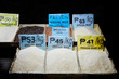 Array of different sorts of dry rice openly displayed in wooden boxes at a public market in Iloilo, Philippines, Asia; big price signs displayed.