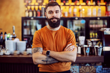 Young Handsome Bearded Tattooed Cafe Owner Standing With Arms Crossed And Looking At Camera.