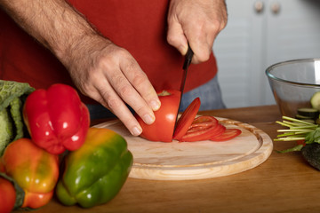 Chef's hands cutting red fresh tomato on a wooden board.