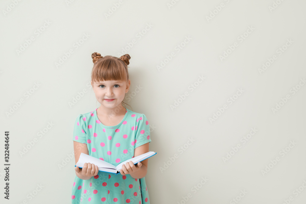 Cute little girl with book on light background