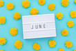 Text June on light box and yellow dandelions on blue background. Concept hello summer. Top view Flat lay.
