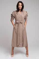 Full length of beautiful brunette young woman wearing long trench coat against grey background. Fashion and style concept