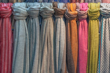Fabric Scarves And Shawls Of Different Colors, Textures And Patterns Are Hung Vertically. Background Image.