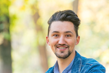 Handsome young man looking at the camera. Portrait of laughing confident and successful young man with a denim jacket and blue shirt outside. Happy guy smiling