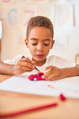 Wall Mural - Beautiful african american toddler sitting painting car toy using marker pen on desk at kindergarten