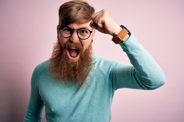 Canvas Print - Handsome Irish redhead man with beard wearing glasses over pink isolated background angry and mad raising fist frustrated and furious while shouting with anger. Rage and aggressive concept.