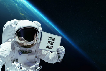spaceman in open space shows a card with your text here on the background of planet earth. astronaut