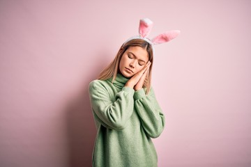 Young beautiful woman wearing easter rabbit ears standing over isolated pink background sleeping tired dreaming and posing with hands together while smiling with closed eyes.