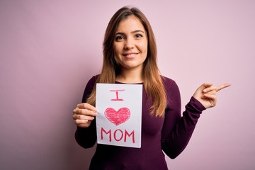 Canvas Print - Young beautiful woman holding paper with love mom message celebrating mothers day very happy pointing with hand and finger to the side