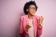 © Krakenimages.com - Young beautiful African American afro businesswoman with curly hair wearing pink jacket celebrating surprised and amazed for success with arms raised and eyes closed. Winner concept.