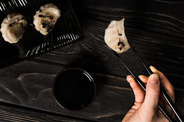 Wall Mural - partial view of woman eating delicious Chinese boiled dumpling with chopsticks and soy sauce at black wooden table