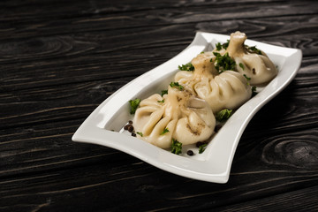 delicious Khinkali with cilantro on plate on black wooden table