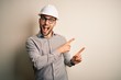 © Krakenimages.com - Young architect man wearing builder safety helmet over isolated background smiling and looking at the camera pointing with two hands and fingers to the side.