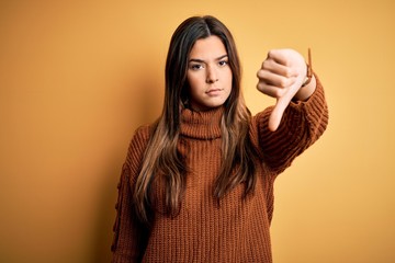 Canvas Print - Young beautiful girl wearing casual sweater standing over isolated yellow background looking unhappy and angry showing rejection and negative with thumbs down gesture. Bad expression.