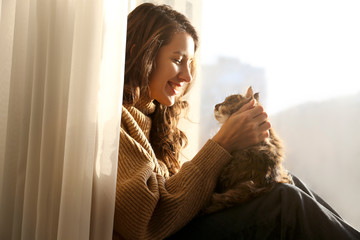 Portrait of young woman holding cute siberian cat with green eyes. Female hugging her cute long hair kitty. Background, copy space, close up. Adorable domestic pet concept.